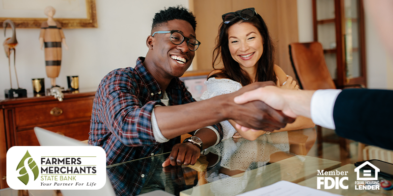 Smiling man shaking hands with out of view person while woman next to him smiles on