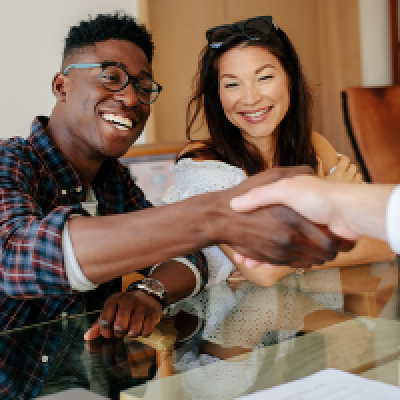 Smiling man shaking hands with out of view person while woman next to him smiles on